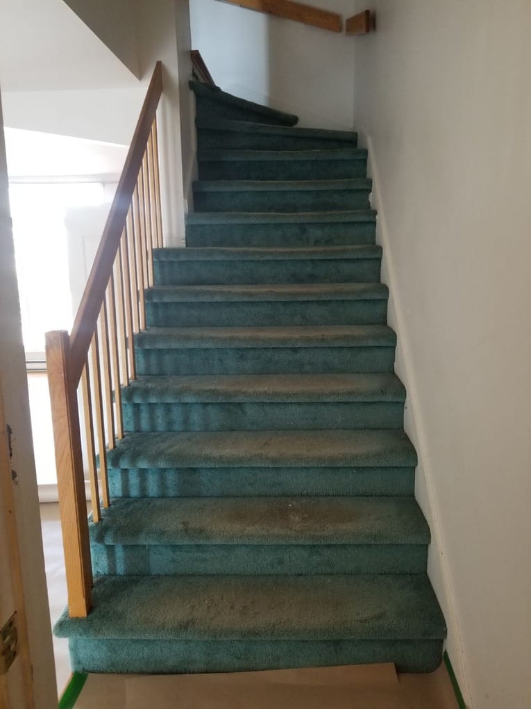 Before: staircase covered in worn teal carpet with a dated wood railing