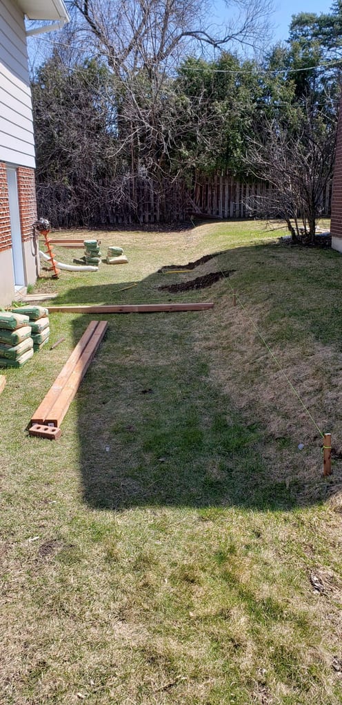 Before: back yard with a leaning grey fence, stacked sod and lumber ready for the build